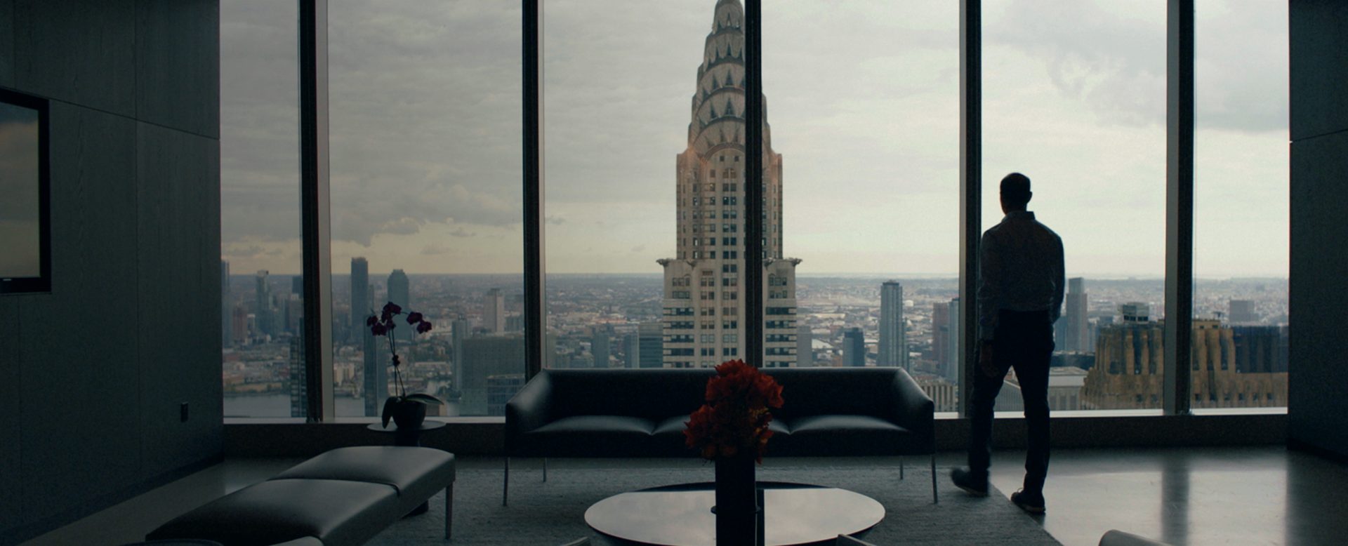 Man standing in front of a window of a skyscraper and looking at the Chrysler Building in New York.