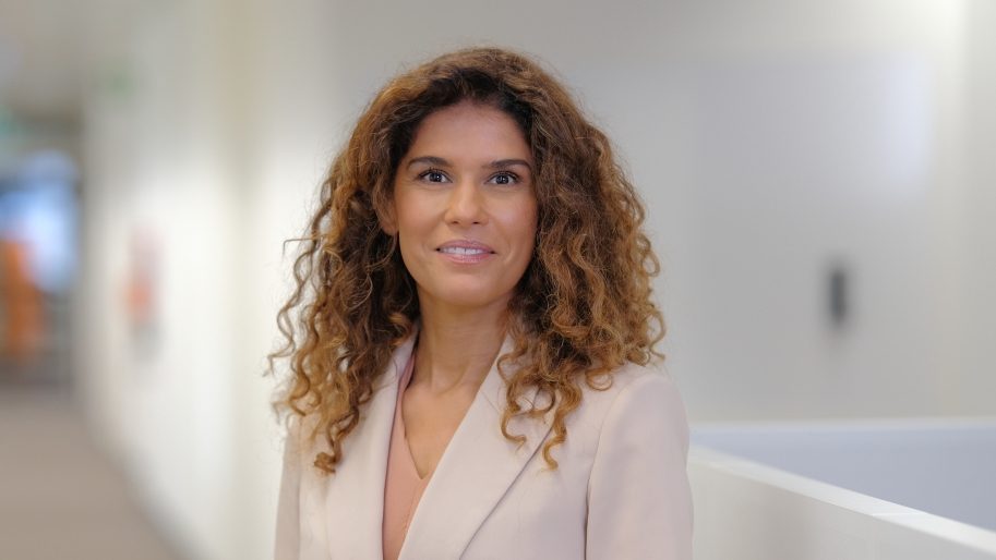 Caucasian lady with blonde curls wearing a business attire indoors.
