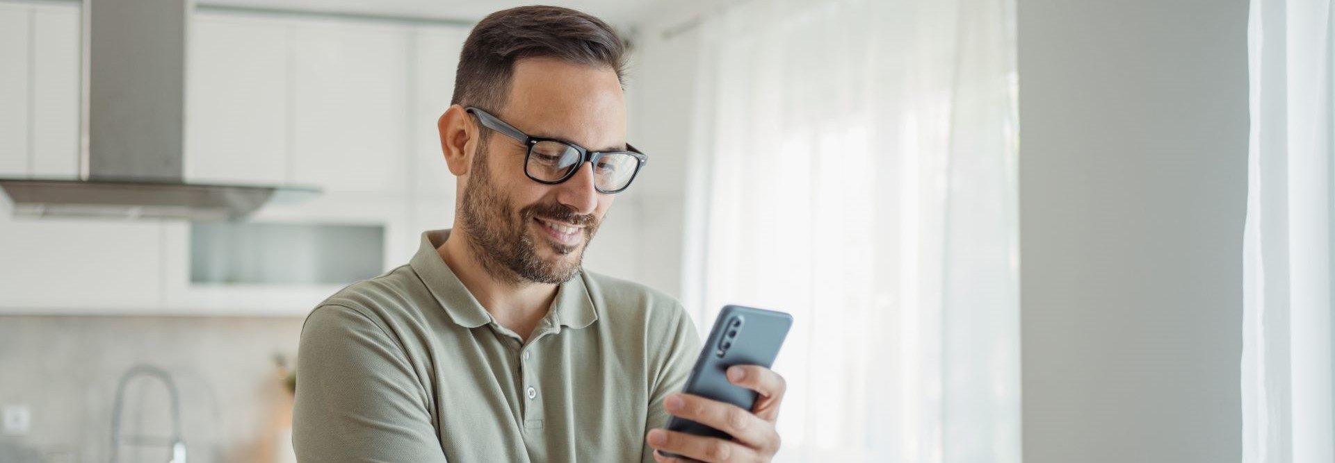 A person holding a smartphone in a modern kitchen environment.