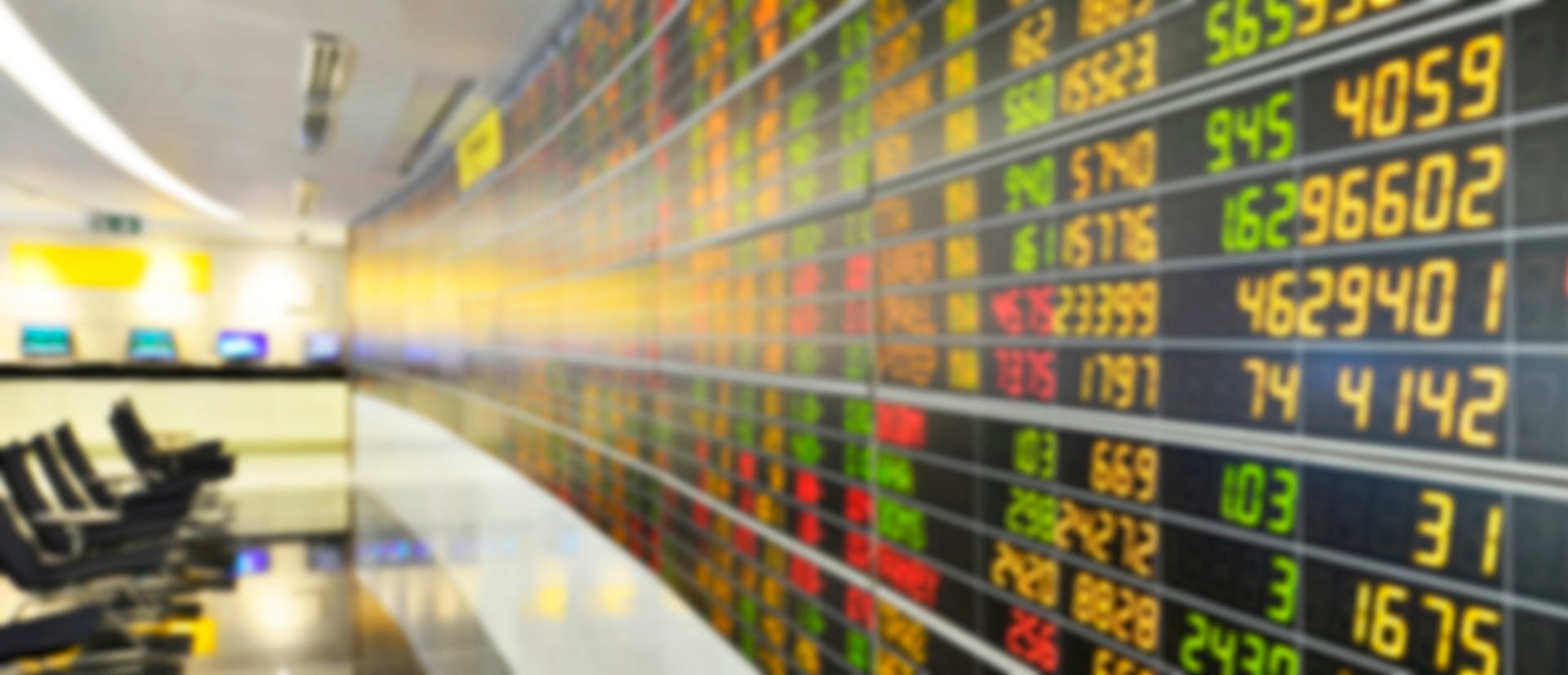 The image depicts a stock trading floor, characterized by several features:
1. **Stock Market Display Boards:** The large electronic boards display various stock tickers, prices, and indices that are essential for traders to make investment decisions. The numbers are lit up in different colors (typically green for increases, red for decreases) indicating the performance of stocks.
2. **Trading Environment:** The layout of the space with desks or terminals where traders might sit and work, surrounded by technology and screens to monitor real-time market data.
3. **Dynamic Atmosphere:** It suggests an environment that's fast-paced and driven by constant changes, typical of trading floors where decisions must be made quickly based on fluctuating data.
4. **Sophisticated Infrastructure:** The image indicates a sophisticated setup involving advanced equipment and infrastructure, essential for the operations of financial markets.
This scene is typical to stock exchanges or financial institutions around the globe, like Wall Street in New York, the London Stock Exchange, or any major financial hubs.