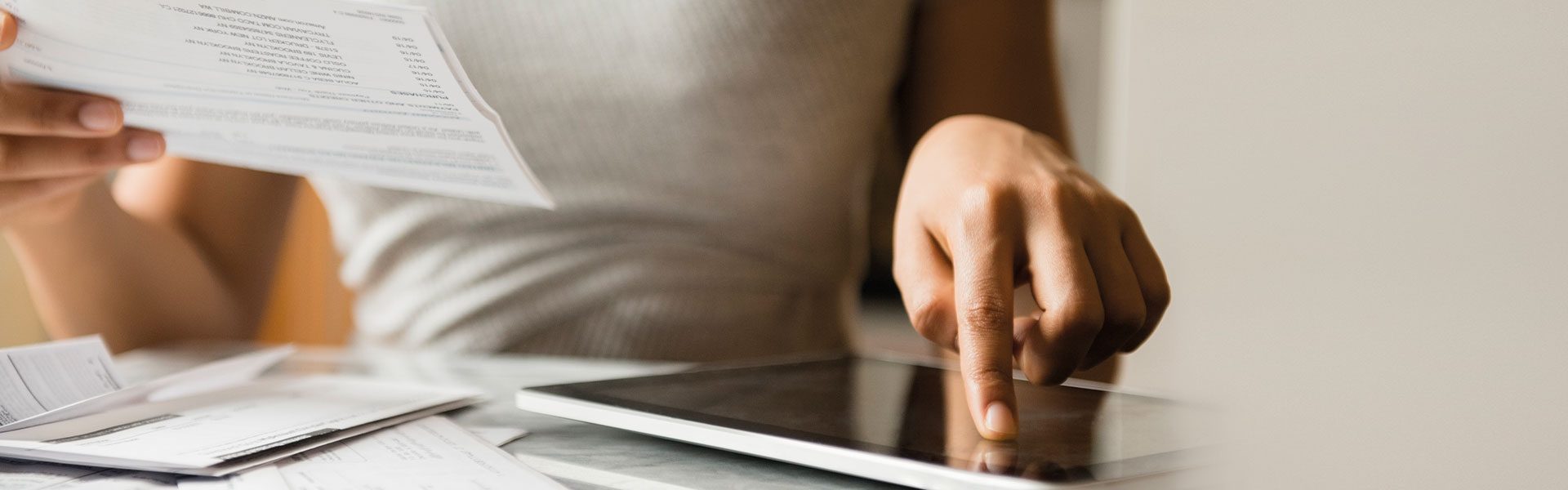 The image shows a person engaged in a task involving paperwork and a tablet.
Details:
- **Person:**
- Appears to be an adult, wearing a casual sleeveless top.
- **Actions:**
- Holding a piece of paper in one hand, suggesting reading or reviewing contents.
- Using the other hand to interact with a tablet, indicating multitasking or digital management of information.
- **Background:**
- Simple and neutral, focusing attention on the person's actions with the paper and tablet.
---
### Implications:
The image evokes a sense of productivity, perhaps related to managing finances, making notes, or organizing tasks digitally. It blends traditional paper-based work with modern technological resources, illustrating versatility in workflows.