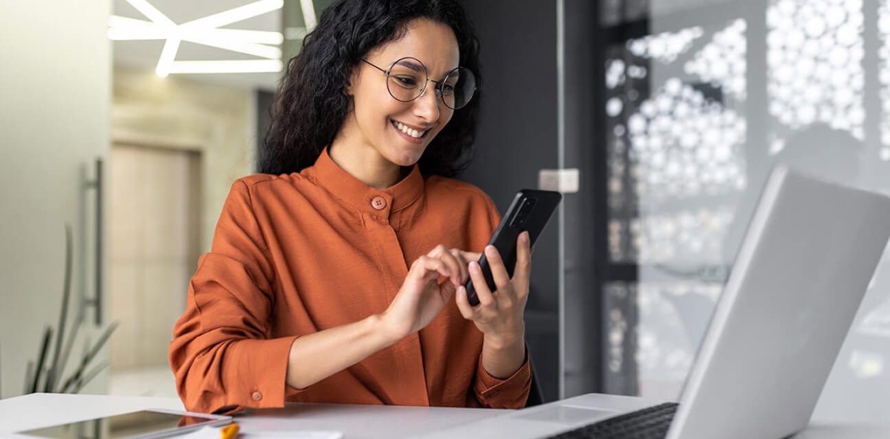 Good news from DZ BANK HR: A woman is smiling at a message on her smartphone, in the background office environment