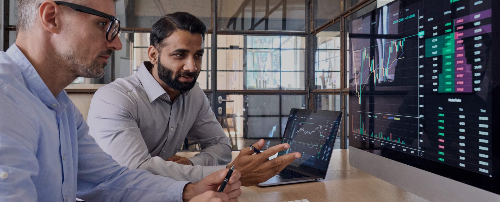 International teams,  international expertise:  two colleagues having a look  at a computer screen that displays  a share price development